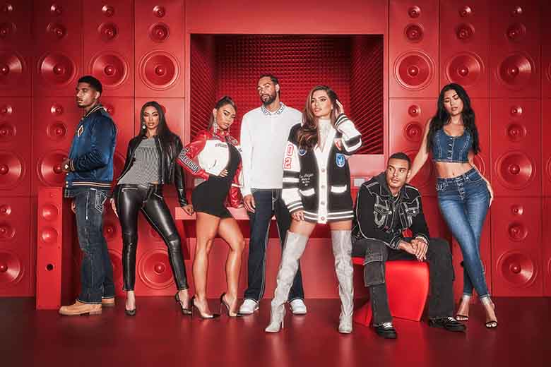 Group of True Religion stylishly dressed individuals posing in front of a vibrant red wall with speaker-like patterns, showcasing a mix of modern streetwear and casual outfits including jackets, skirts, jeans, and boots.