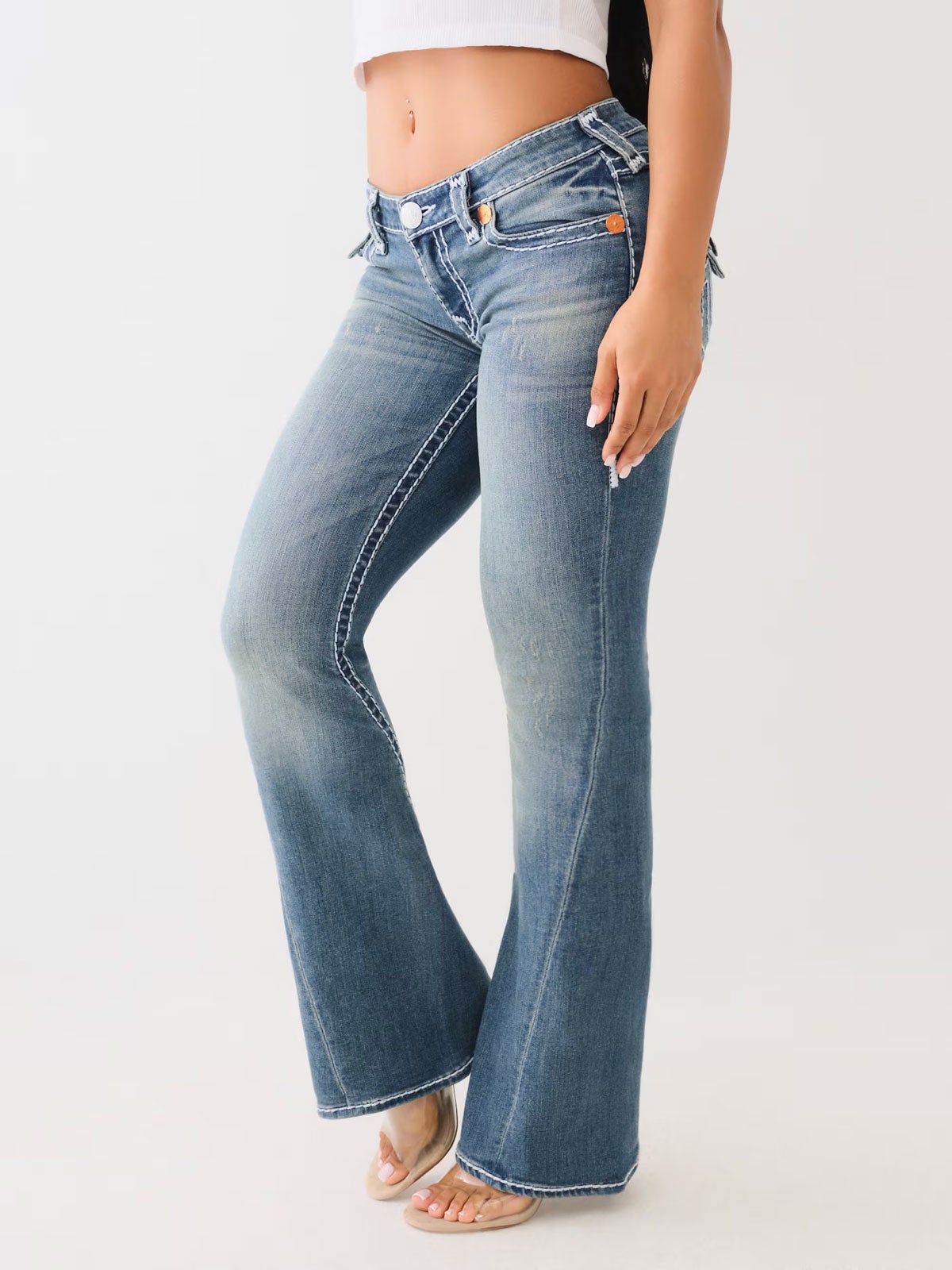 Woman wearing True Religion medium wash boot cut jeans with a zipper hem and clear high heels