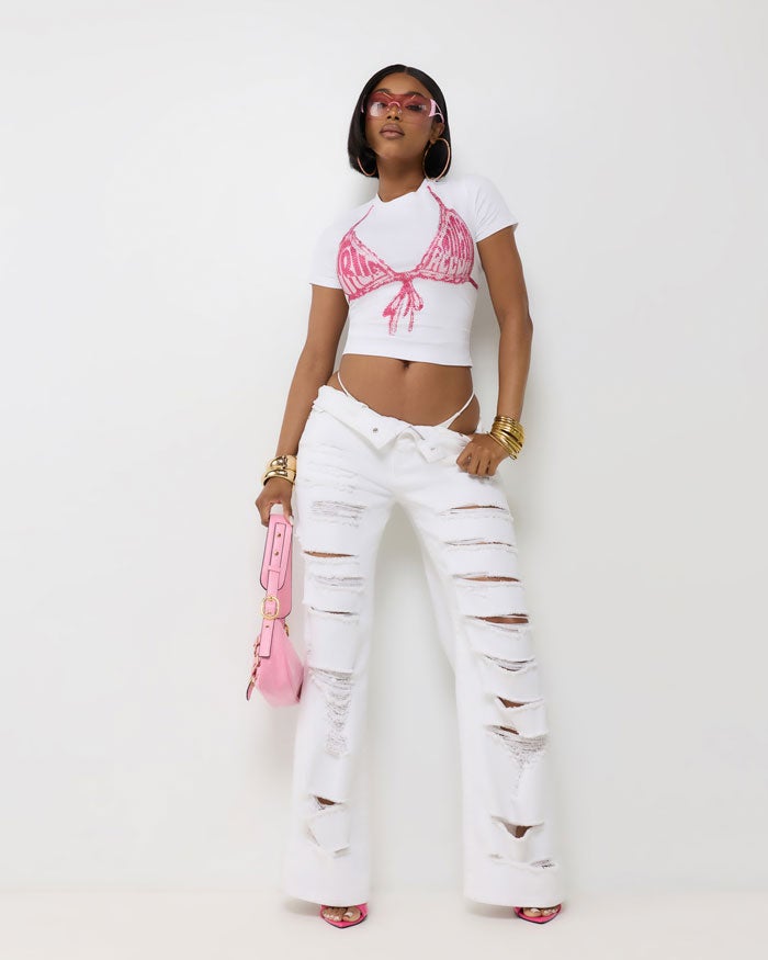 Woman standing in front of a white backdrop wearing ripped white jeans and a white true religion t-shirt with a faux bikini top on it.