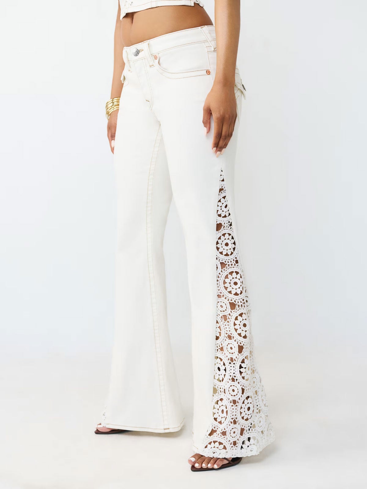 View of a woman’s legs in front of a white backdrop wearing white flare jeans with lace panel down the side 