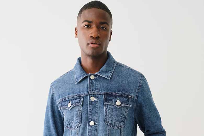 Man wears a blue true religion denim jacket with silver buttons and blue jeans.